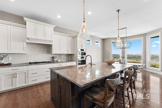 5557 E Hootowl Dr, Boise, ID 83716 - kitchen featuring decorative backsplash, white cabinets, dark wood-style flooring, stainless steel appliances, and an island with sink
