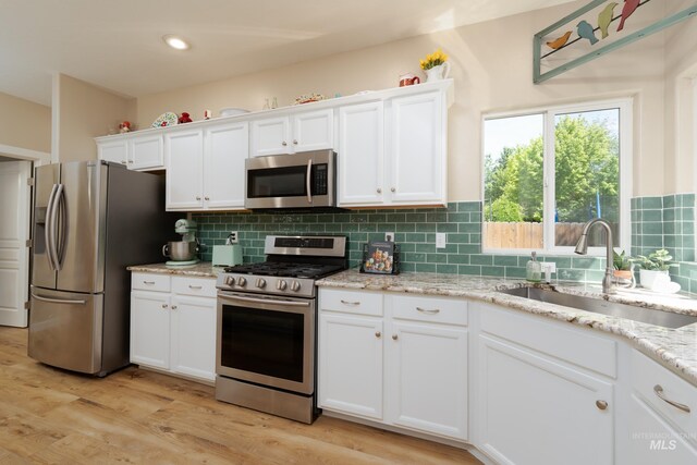 6524 S Derbyshire Ave, Boise, ID 83709 - kitchen featuring appliances with stainless steel finishes, a sink, white cabinetry, light wood-type flooring, and tasteful backsplash