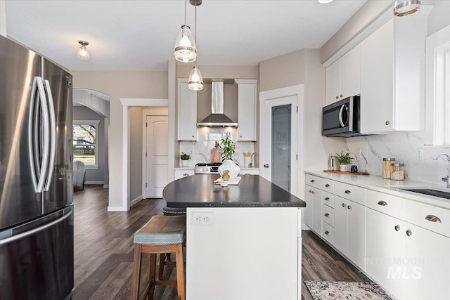 kitchen with appliances with stainless steel finishes, white cabinets, a kitchen island, sink, and wall chimney exhaust hood