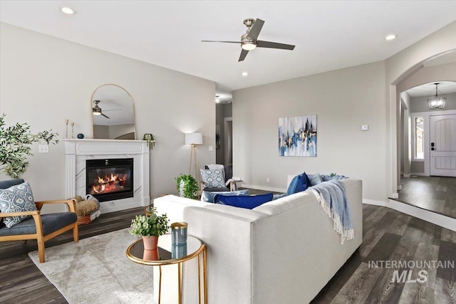 living room with ceiling fan, a high end fireplace, and dark hardwood / wood-style flooring