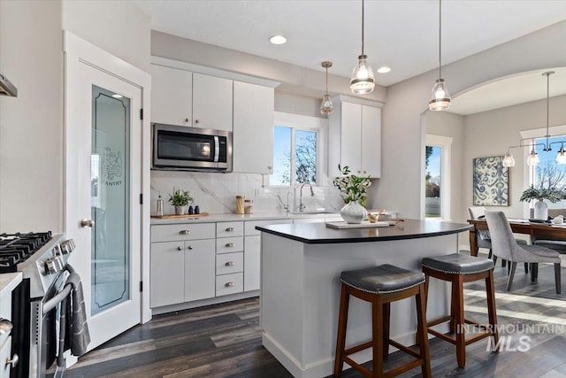 kitchen with tasteful backsplash, white cabinetry, pendant lighting, dark hardwood / wood-style flooring, and stainless steel appliances