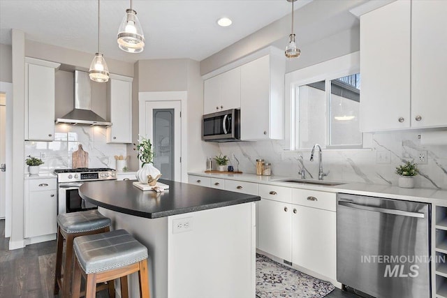 kitchen with white cabinets, appliances with stainless steel finishes, a center island, wall chimney exhaust hood, and sink