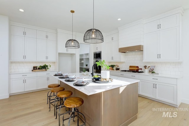 kitchen featuring appliances with stainless steel finishes, light hardwood / wood-style flooring, white cabinetry, hanging light fixtures, and an island with sink