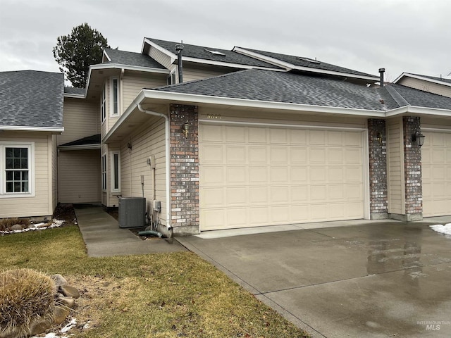 view of side of home with a garage, concrete driveway, brick siding, and central AC unit