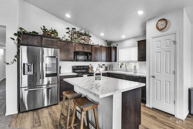 kitchen featuring dark brown cabinetry, light countertops, a center island, wood finished floors, and black appliances