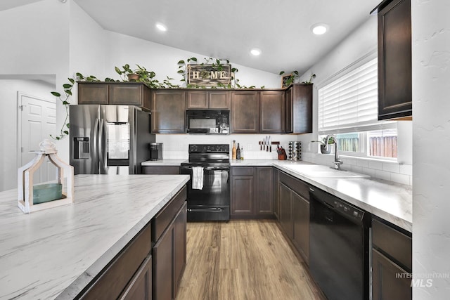 kitchen featuring dark brown cabinets, a sink, light wood-style floors, lofted ceiling, and black appliances