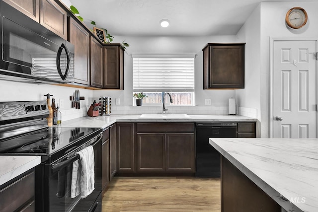 kitchen with dark brown cabinetry, light wood-type flooring, light stone counters, a sink, and black appliances
