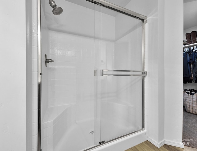 bathroom with wood finished floors, a spacious closet, and a shower stall