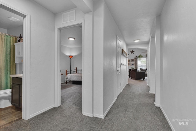hall with baseboards, dark carpet, and visible vents