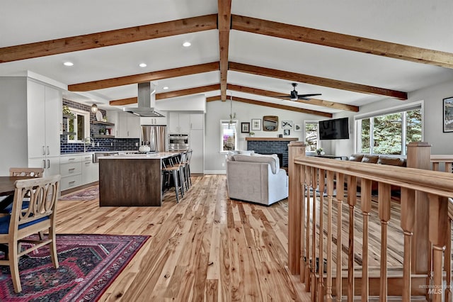 living room with lofted ceiling with beams, a ceiling fan, a fireplace, recessed lighting, and light wood-style flooring