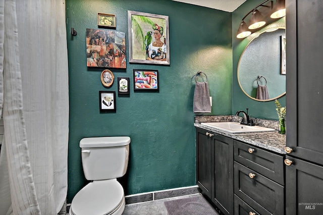 full bath featuring toilet, a textured wall, baseboards, and vanity