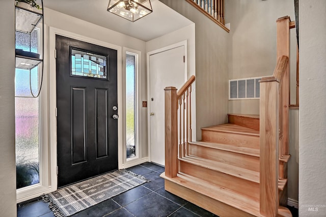 entrance foyer with visible vents, dark tile patterned floors, and stairway