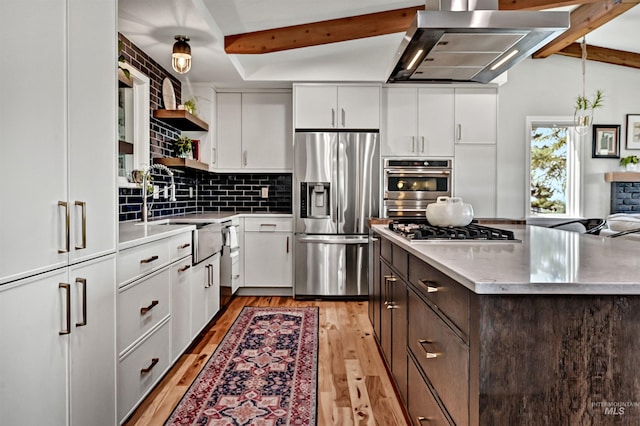 kitchen with wall chimney exhaust hood, light wood-type flooring, dark brown cabinets, appliances with stainless steel finishes, and a sink