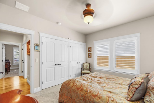 bedroom featuring ceiling fan, light colored carpet, visible vents, baseboards, and two closets