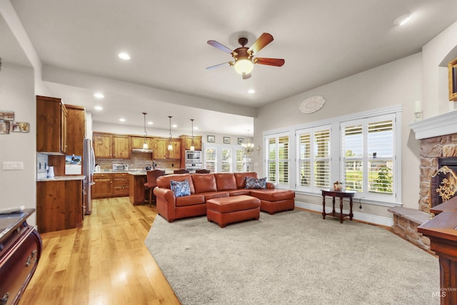 living room featuring a healthy amount of sunlight, light wood finished floors, a fireplace, and ceiling fan with notable chandelier