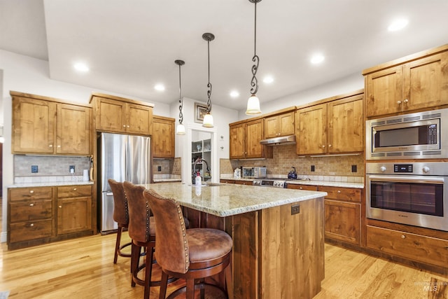 kitchen with brown cabinetry, stainless steel appliances, light wood-type flooring, under cabinet range hood, and a sink