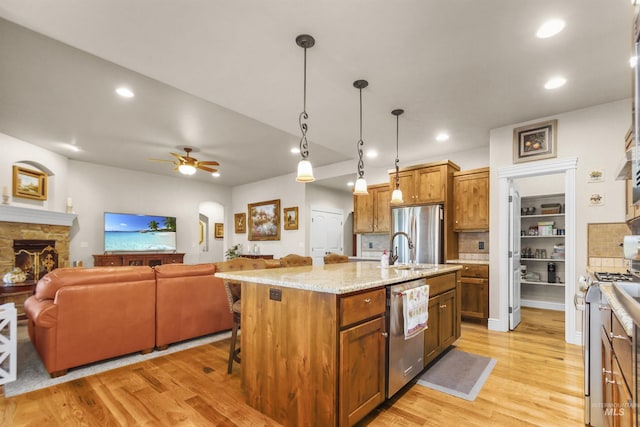 kitchen with light wood-style flooring, a kitchen breakfast bar, open floor plan, stainless steel appliances, and a stone fireplace