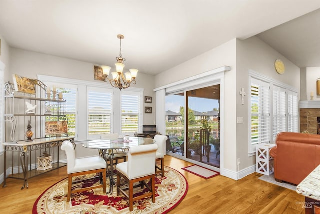 dining area with light wood-style floors, a chandelier, a stone fireplace, and baseboards