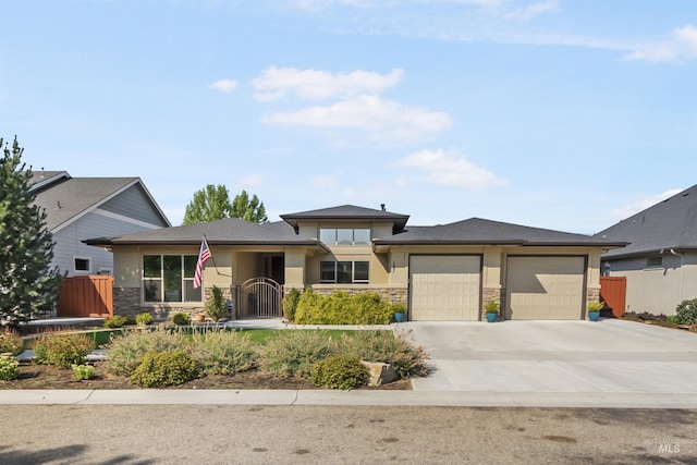 prairie-style house featuring an attached garage, stone siding, driveway, a gate, and stucco siding