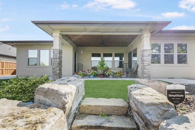 view of front of house with ceiling fan, a porch, fence, stucco siding, and a front yard