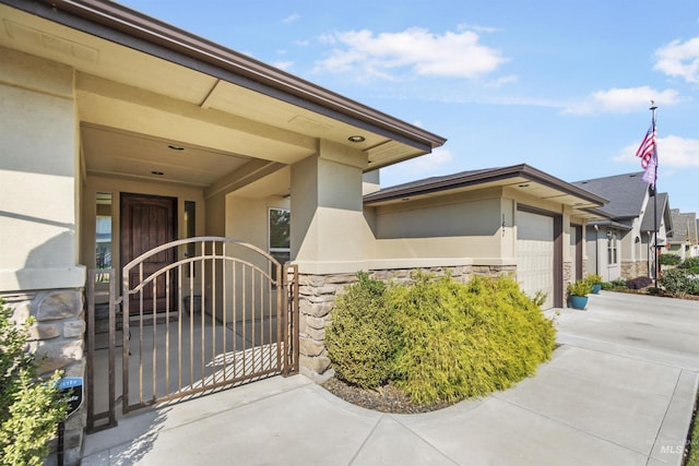 view of exterior entry featuring concrete driveway, stone siding, an attached garage, a gate, and stucco siding