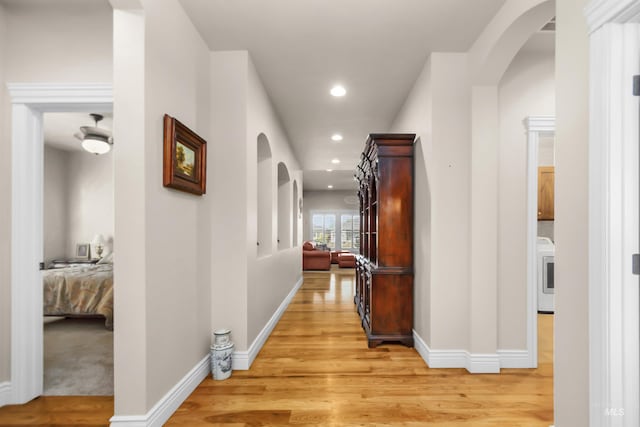 hallway with arched walkways, washer / clothes dryer, and light wood-style flooring