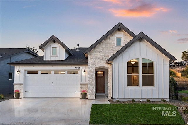 view of front facade featuring concrete driveway, board and batten siding, a front yard, a garage, and stone siding