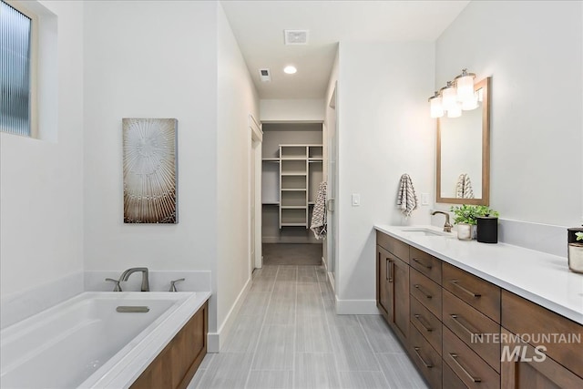 full bathroom with a walk in closet, visible vents, vanity, baseboards, and a bath