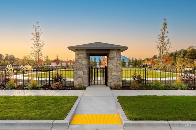 exterior space with stone siding, a gate, fence, and a lawn