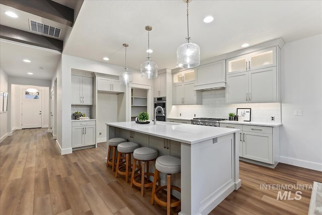 kitchen featuring visible vents, light countertops, a center island with sink, glass insert cabinets, and pendant lighting