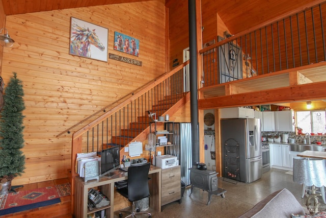 interior space featuring a wood stove, wood walls, sink, and high vaulted ceiling