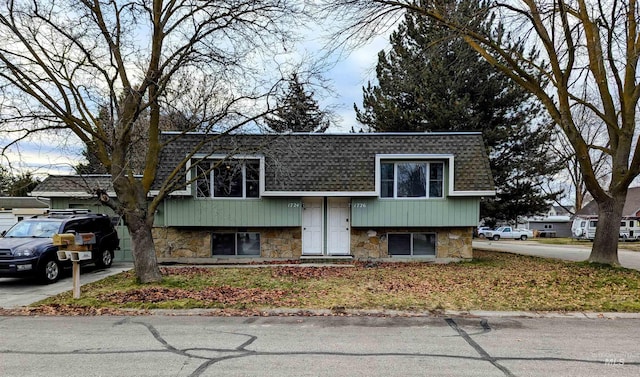 view of front of home featuring stone siding, mansard roof, and roof with shingles