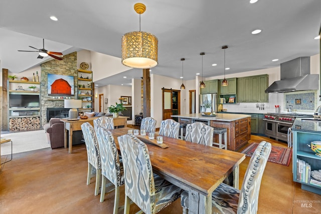 dining space featuring ceiling fan, a barn door, a fireplace, and vaulted ceiling