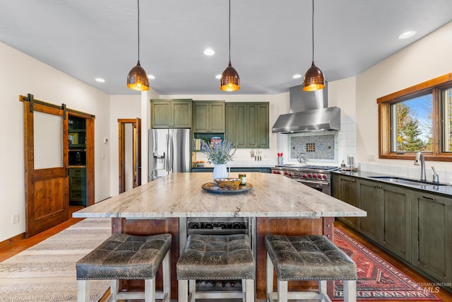 kitchen with a center island, wall chimney range hood, sink, a barn door, and stainless steel appliances