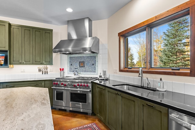 kitchen with sink, stainless steel appliances, wall chimney range hood, light stone counters, and green cabinetry