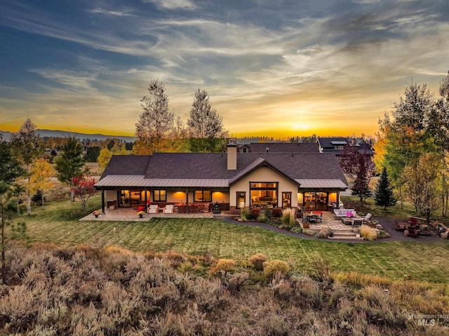 back house at dusk featuring a yard, an outdoor hangout area, and a patio