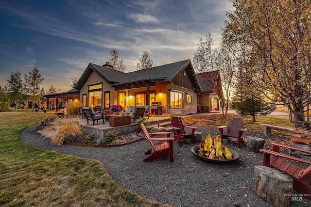 back house at dusk featuring a patio and an outdoor living space with a fire pit