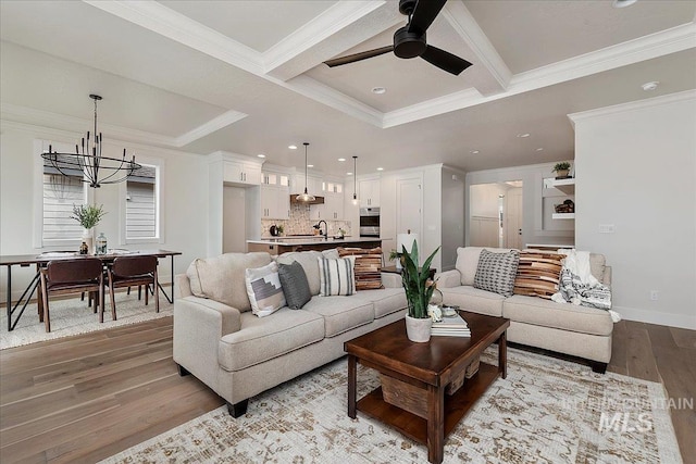 living room with coffered ceiling, ceiling fan with notable chandelier, crown molding, sink, and light hardwood / wood-style floors