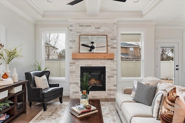 sitting room featuring hardwood / wood-style floors, crown molding, ceiling fan, a fireplace, and beamed ceiling