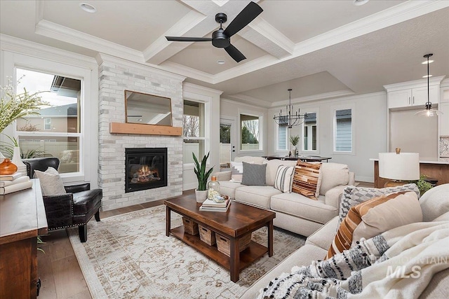 living room featuring ceiling fan with notable chandelier, crown molding, a brick fireplace, light wood-type flooring, and beam ceiling