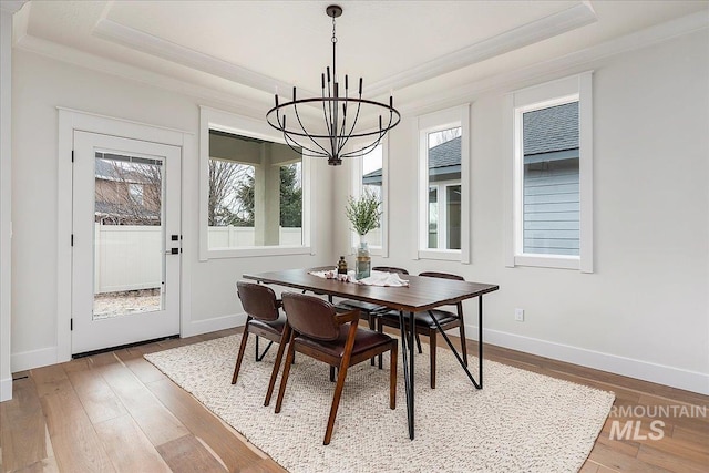 dining area with a chandelier, wood-type flooring, a tray ceiling, and ornamental molding