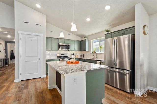 kitchen with appliances with stainless steel finishes, a center island, light stone countertops, decorative light fixtures, and vaulted ceiling