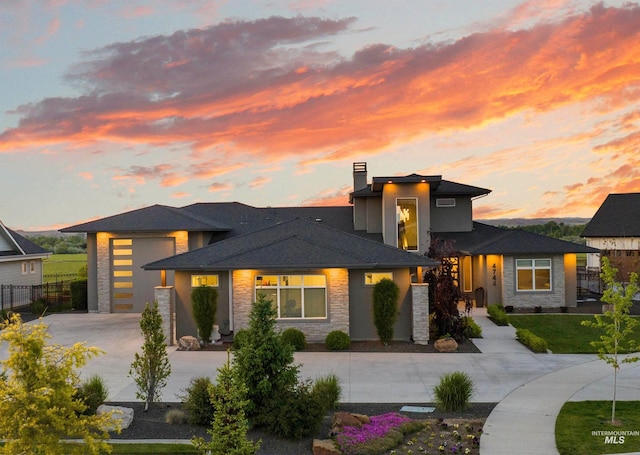 prairie-style home featuring fence, concrete driveway, a chimney, a garage, and stone siding