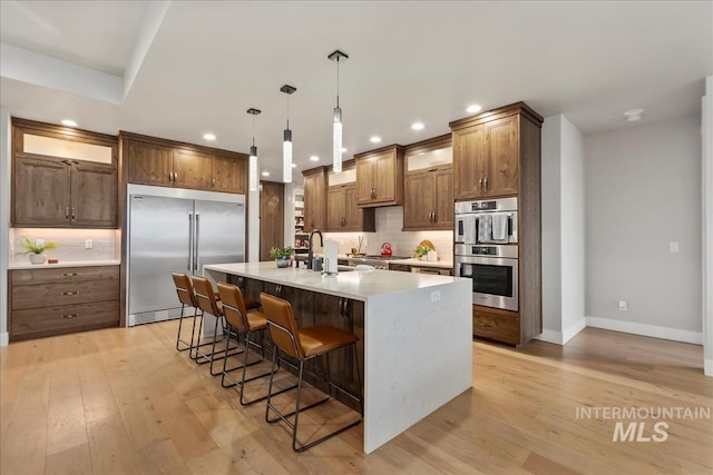 kitchen with a breakfast bar, light wood-style flooring, tasteful backsplash, and appliances with stainless steel finishes