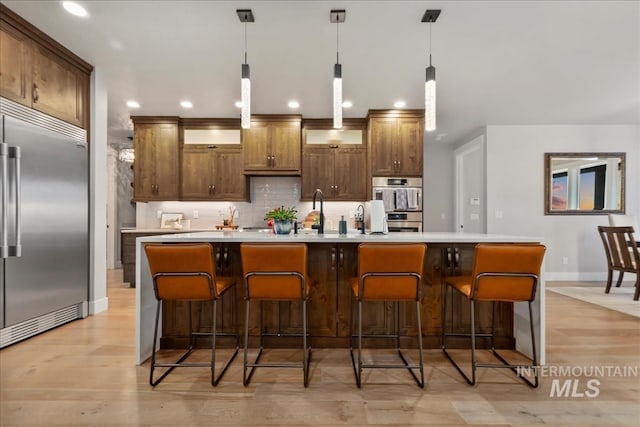 kitchen with backsplash, decorative light fixtures, light countertops, a large island with sink, and appliances with stainless steel finishes