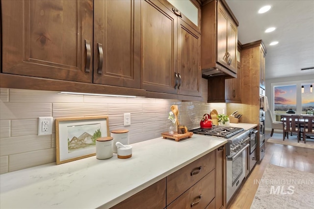 kitchen with high end range, recessed lighting, light wood-style flooring, and backsplash