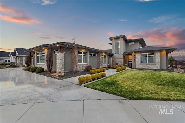 prairie-style house with stucco siding, stone siding, a lawn, and concrete driveway