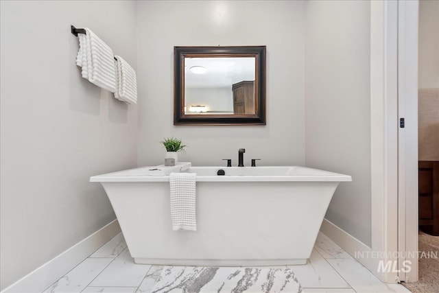 bathroom with a freestanding tub, baseboards, and marble finish floor