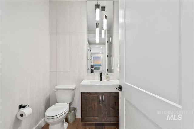 half bath with toilet, tile walls, and vanity