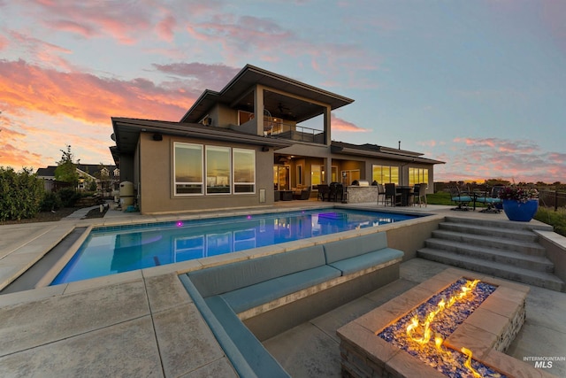 back of property at dusk with stucco siding, outdoor dining area, a balcony, a fenced in pool, and a patio area